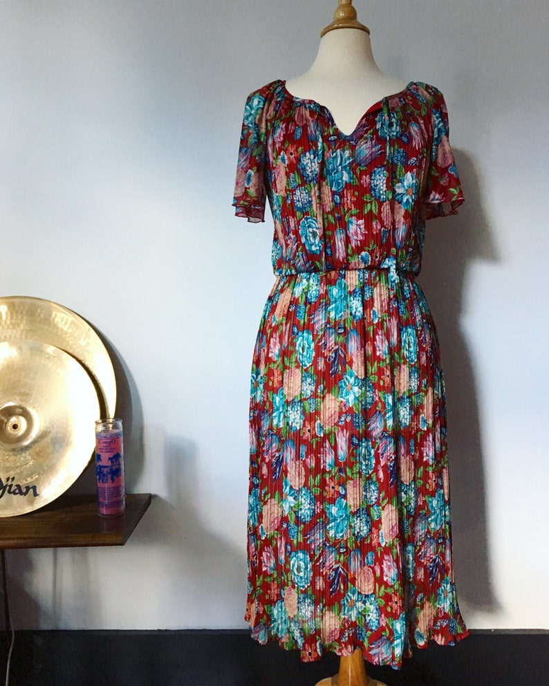 May include: A red, blue, and green floral print midi dress with a ruffled neckline and short sleeves. The dress has a fitted bodice and a flowing skirt.