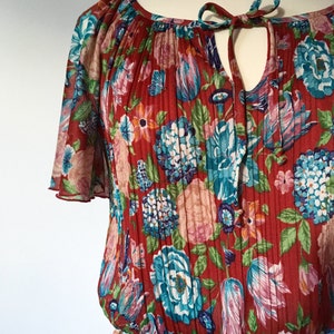 May include: A red floral print dress with a gathered neckline and short sleeves. The dress has a tie at the neckline and a pleated skirt.