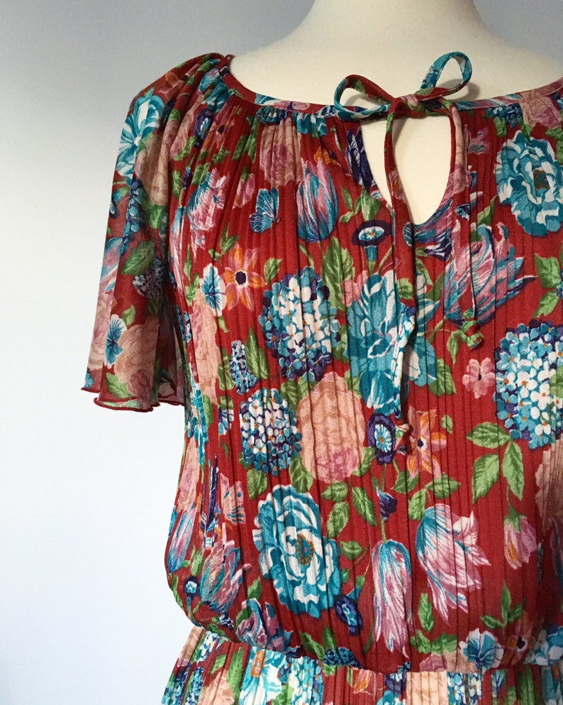 May include: A red floral print dress with a gathered neckline and short sleeves. The dress has a tie at the neckline and a pleated skirt.