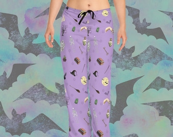 May include: Lavender pajama pants with a black drawstring. The pants feature a repeating pattern of Halloween-themed illustrations, including skeletons, potion bottles, witch hats, moons, and books. The background has a watercolor effect with bat silhouettes.