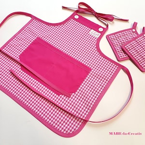 Può includere: Un set di grembiule rosa e bianco a quadretti con presine abbinate. Il grembiule ha una grande tasca e il nome "LEA" è stampato in alto. Il set è rifinito in rosa e ha lacci rosa.