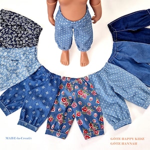 May include: A set of eight pairs of denim doll pants in various patterns, including floral, polka dot, and geometric designs. The pants are all blue and white and have a gathered elastic waistband. The text "Götz Happy Kidz Götz Hannah" is visible in the bottom right corner of the image.