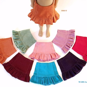 Könnte beinhalten: Ein Set aus acht Cord-Puppenröcken in verschiedenen Farben, darunter Orange, Grün, Rosa, Rot, Burgunder, Türkis, Lila und Braun. Jeder Rock hat einen Rüschen-Saum.