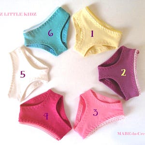 Könnte beinhalten: Sechs Paar Puppenunterhosen, die in einem Kreis angeordnet und mit den Zahlen eins bis sechs beschriftet sind. Die Farben umfassen Gelb, Lila, Pink, Dunkelrosa, Weiß und Türkis. Jedes Paar hat einen dekorativen Zickzack-Saum an den Rändern.
