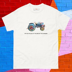 May include: White t-shirt featuring a colorful watercolor painting of a vintage tractor. The tractor is painted in shades of blue, red, yellow, and green. The text "MY POT OF GOLD AT THE END OF THE RAINBOW" is printed below the tractor.