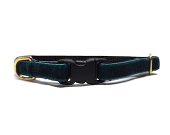 May include: A dark green velvet cat collar with a black plastic buckle and gold-colored metal hardware. The collar is designed to be adjustable and is shown against a white background.