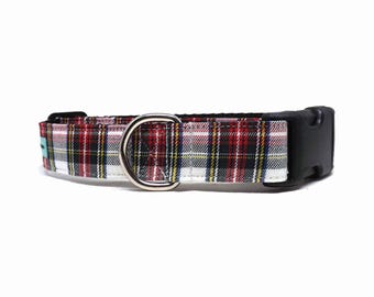 May include: A pet collar featuring a red, white, black, and yellow plaid pattern. The collar includes a black plastic side-release buckle, a silver-toned metal D-ring for leash attachment, and a small teal fabric tag on the side.