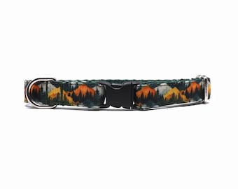 May include: A dog collar with a mountain range pattern in shades of green, orange, and yellow. The collar has a black plastic buckle and a silver metal D-ring for leash attachment. The overall design is outdoorsy.