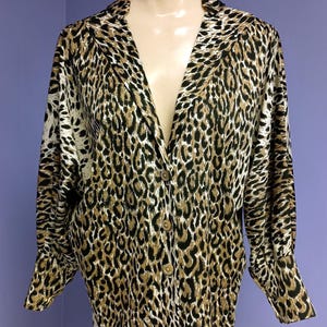 May include: A button-down shirt with a leopard print design. The long-sleeved shirt features a classic collar and is displayed on a mannequin. The print includes black, brown, and cream colors.