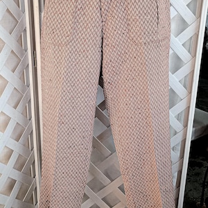 Puede incluir: Pantalones vintage marrones y beiges con estampado de espiga, cintura alta y detalles de botones. Los pantalones tienen dos bolsillos delanteros con botones rojos y un cierre de botón a juego en la cintura. Los pantalones se muestran sobre un fondo de celosía blanca.