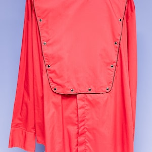 Puede incluir: Una camisa roja de manga larga con ribete negro y tachuelas plateadas alrededor del cuello y la parte superior.