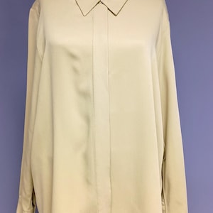 Puede incluir: Camisa abotonada de manga larga de color amarillo pálido con cuello clásico, expuesta sobre un maniquí. La tela parece suave y ligera. La camisa tiene un corte entallado. Adecuada para diversas ocasiones. La camisa es de color amarillo claro.