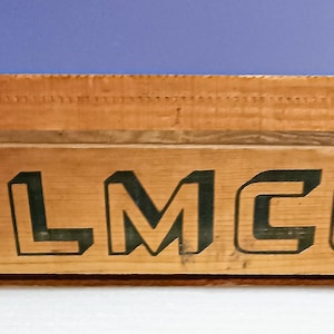 May include: A wooden crate with the word "ELMC0" painted in green letters on the front. The crate is made of natural wood and has a rustic look.
