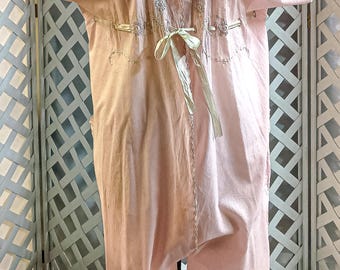 Puede incluir: Un mono vintage rosa claro con mangas cortas y cuello en V. El mono presenta detalles bordados alrededor del escote y las mangas, con una cinta en la cintura. La parte inferior es de corte holgado.