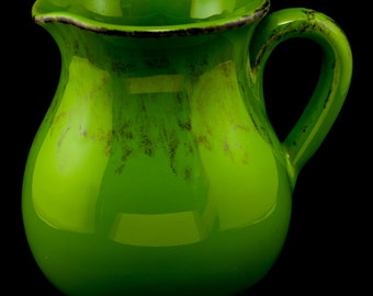 May include: A green ceramic pitcher with a speckled glaze. The pitcher has a rounded body and a handle.
