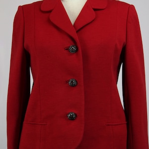 Puede incluir: Una chaqueta roja con cuello de muesca y tres botones negros. La chaqueta tiene una silueta ajustada y mangas largas.