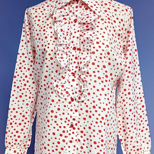 May include: A white long-sleeved button-up shirt with a ruffled collar and red polka dots.