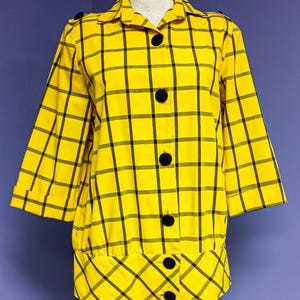 May include: A yellow jacket with a black plaid pattern. The jacket has three-quarter sleeves, a collar, and large black buttons down the front. The bottom of the jacket has a unique, flared design. The jacket is displayed on a mannequin.