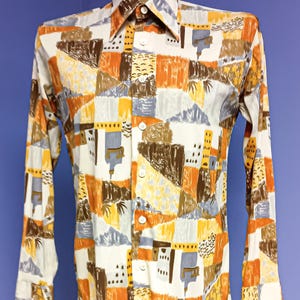May include: A long-sleeved shirt with a colourful geometric pattern in shades of orange, brown, yellow, and grey. The shirt has a classic collar and buttoned cuffs. The shirt is displayed on a mannequin.