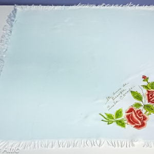 May include: A light blue square handkerchief with a white fringe border. The handkerchief features a floral design of red roses and green leaves in the corner, with the text "Ste Anne de Beaupre, Quebec Canada."