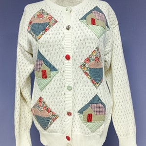 Peut inclure: Un cardigan blanc en tricot avec une fermeture boutonnée et un motif patchwork. Les patchs sont faits de différents tissus et présentent des motifs floraux, des maisons et des formes géométriques. Le cardigan a un tricot texturé et une coupe décontractée.