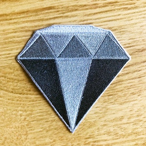 Puede incluir: Un parche bordado en forma de diamante plateado y negro.