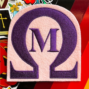 Op de afbeelding: Paarse geborduurde patch met een roze achtergrond. De patch heeft een gestileerde letter M in een paars omega-symbool.