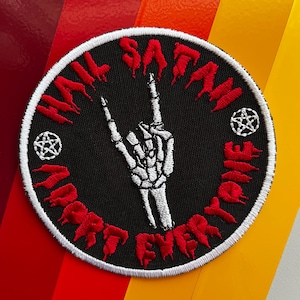 Könnte beinhalten: Ein schwarzer und weißer gestickter Patch mit einer roten, tropfenden Schrift, die "Hail Satan Adore Everything" lautet. Der Patch zeigt eine weiße Skeletthand, die die Rock'n'Roll-Handgeste macht, mit einem Pentagramm auf jeder Seite der Hand.