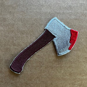 May include: An embroidered axe patch in grey and red. The axe head is grey with a red edge. The handle is brown.