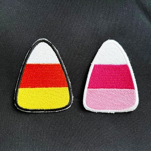 Op de afbeelding: Twee geborduurde candy corn-patches, een met rode, gele en witte strepen en de andere met roze en witte strepen.