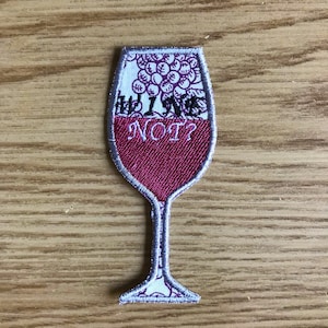 May include: Embroidered iron-on patch of a wine glass with the text "Why Wine Not?" in black lettering. The glass is filled with red wine and has a white background with a grape design.