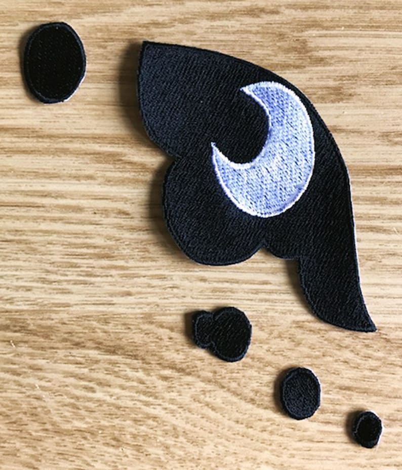 Pu&ograve; includere: Toppa in feltro nero da stirare con una mezzaluna bianca e un interno viola. Ci sono quattro piccoli cerchi in feltro nero.