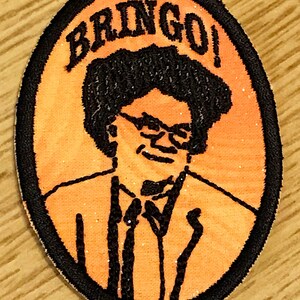 Op de afbeelding: Oranje en zwarte geborduurde patch met een cartoon afbeelding van een man met een bril en de tekst "BRINGO!"