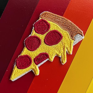 Puede incluir: Parche bordado de una porción de pizza con corteza amarilla, pepperoni rojo y borde de corteza marrón. El parche tiene un borde blanco y un efecto de queso goteando. El fondo presenta un degradado de colores rojo y amarillo.