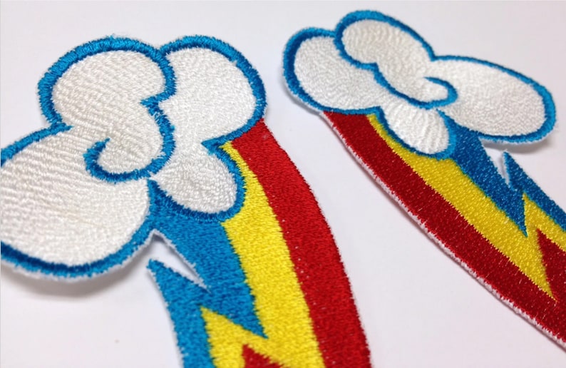 Op de afbeelding: Twee geborduurde strijkpatches met een witte wolk met een blauwe omtrek en een regenboog met rode, gele en blauwe strepen. De regenboog is gevormd als een bliksem.