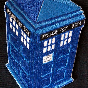 May include: A blue embroidered patch of the TARDIS, the time machine from the Doctor Who television series. The patch features the iconic blue box shape with a white door and windows, and the text "POLICE BOX" on the side.