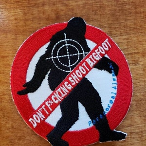 Op de afbeelding: Een geborduurde patch met een zwarte silhouet van Bigfoot in een rode cirkel met een doelwit op zijn borst. De tekst "DON'T F*CKING SHOOT BIGFOOT" staat op de patch.