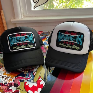 May include: Two black and white baseball caps with the text "the last DRIVE-IN with Joe Bob Briggs" embroidered on the front.