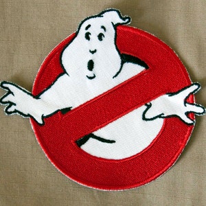 以下が含まれることがあります： ゴーストバスターズのロゴが刺繍された赤と白のパッチ。黒い輪郭の白い幽霊が、斜めに黒い線が引かれた赤い円の中にあります。