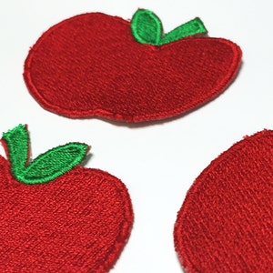 May include: Three red felt apple patches with green felt leaves. The apples are embroidered with a textured surface.