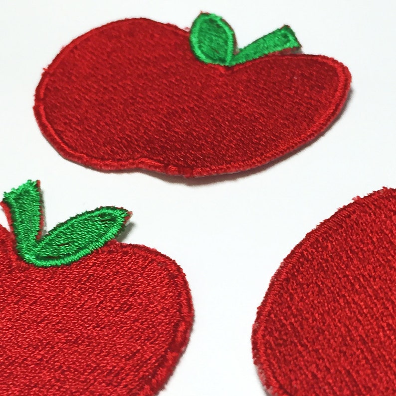 May include: Three red felt apple patches with green felt leaves. The apples are embroidered with a textured surface.
