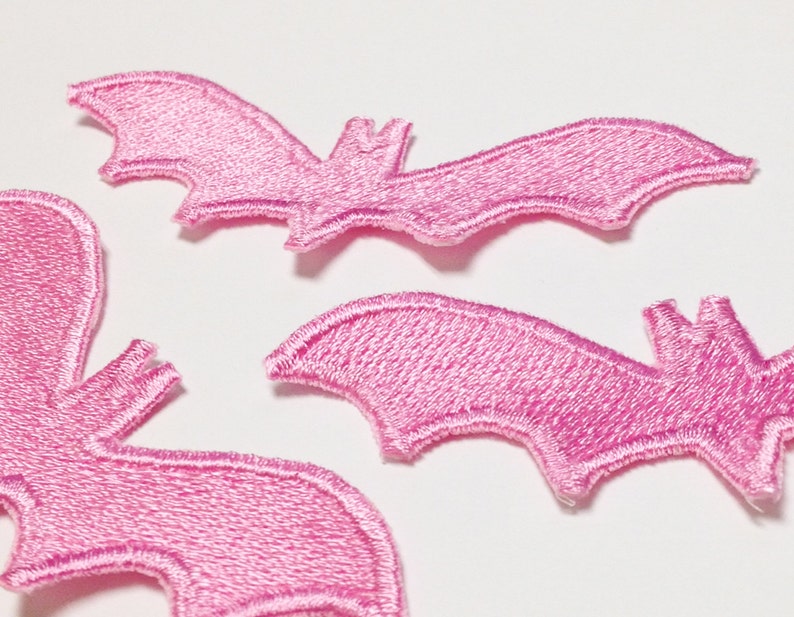May include: Three pink felt bat appliques. The bats are in various sizes and have a stitched outline.