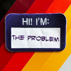 Könnte beinhalten: Ein gestickter Aufnäher in Lila und Weiß mit dem Text "Hi! I'm: The Problem".