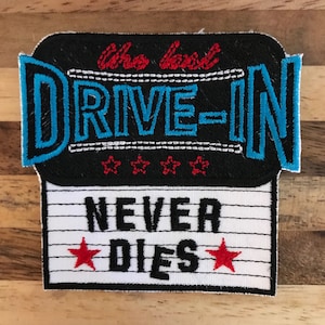 Könnte beinhalten: Ein schwarzer und weißer gestickter Aufnäher mit dem Text "The good DRIVE-IN NEVER DIES" und drei roten Sternen. Der Text "DRIVE-IN" ist in Blau und weiß umrandet.