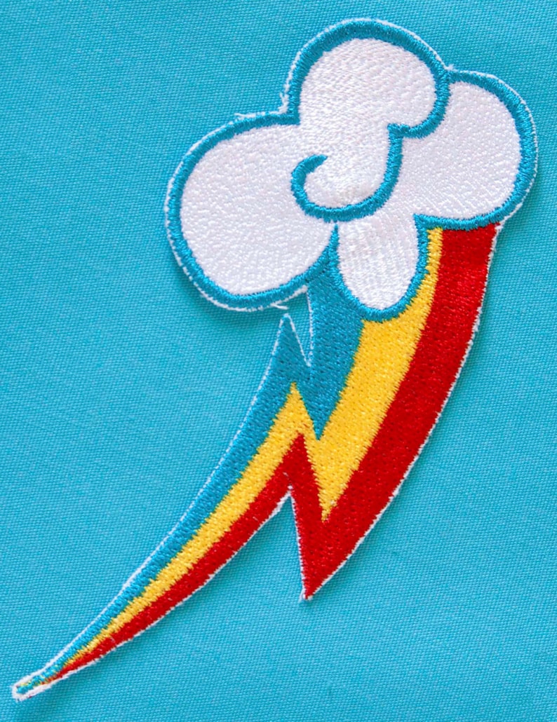 Op de afbeelding: Een witte wolk met een regenboog bliksem, geborduurd op een blauwe stof. De wolk is wit met een blauwe omtrek, en de bliksem is rood, geel en blauw.