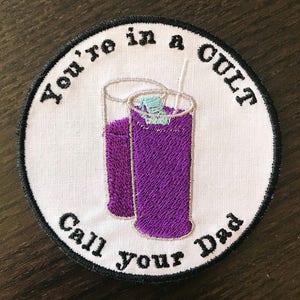 Könnte beinhalten: Weißer gestickter Aufnäher mit schwarzem Text, der "You're in a cult. Call your dad." lautet. Der Aufnäher zeigt zwei lila Gläser mit einem Strohhalm und Eiswürfeln.