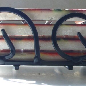 Op de afbeelding: Een zwarte metalen onderzetterhouder met vier witte en rode onderzetters. De houder heeft een uniek ontwerp met twee hoefijzervormige lussen aan elke kant.