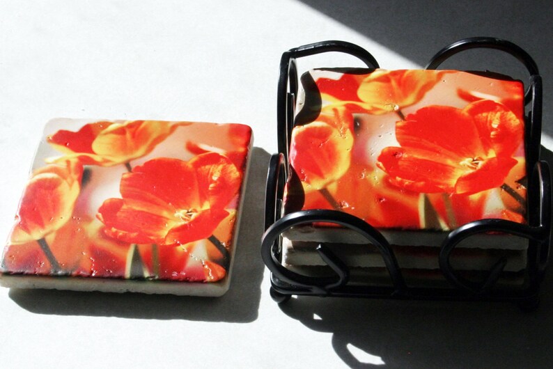 Op de afbeelding: Set van zes oranje en gele bloembedden met een zwarte metalen houder. De onderzetters tonen een close-up afbeelding van oranje en gele tulpen.