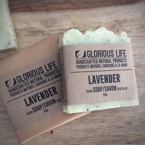 Puede incluir: Dos barras de jab&oacute;n de lavanda hecho a mano envueltas en papel marr&oacute;n con el nombre de la marca "Glorious Life" y el texto "Productos naturales artesanales" y "Jab&oacute;n vegano/Savon" impreso en el embalaje. El jab&oacute;n es de color verde claro y tiene un sutil aroma a lavanda.
