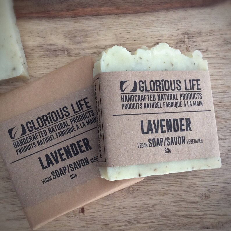 Puede incluir: Dos barras de jab&oacute;n de lavanda hecho a mano envueltas en papel marr&oacute;n con el nombre de la marca "Glorious Life" y el texto "Productos naturales artesanales" y "Jab&oacute;n vegano/Savon" impreso en el embalaje. El jab&oacute;n es de color verde claro y tiene un sutil aroma a lavanda.